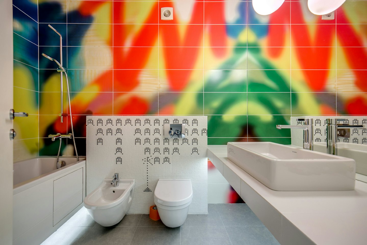 Modernes Badezimmer mit weißen Armaturen und bunten Wandfliesen mit Muster.